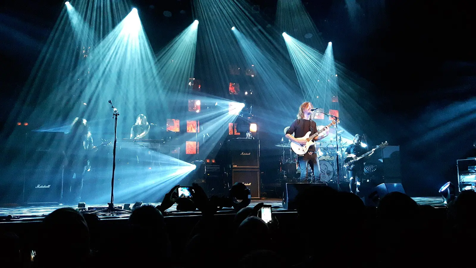 A band plays on the lit stage at the 013 venue in Tilburg, with blue spotlights and the audience in silhouette