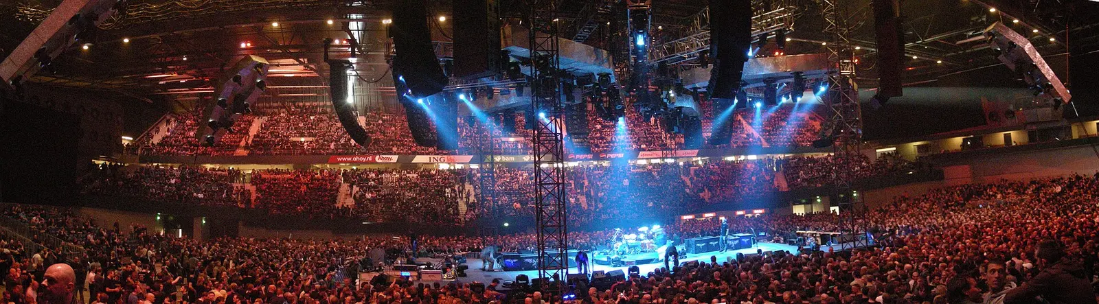 Wide panorama of a packed standing floor and lit stage inside the Rotterdam Ahoy arena during a concert