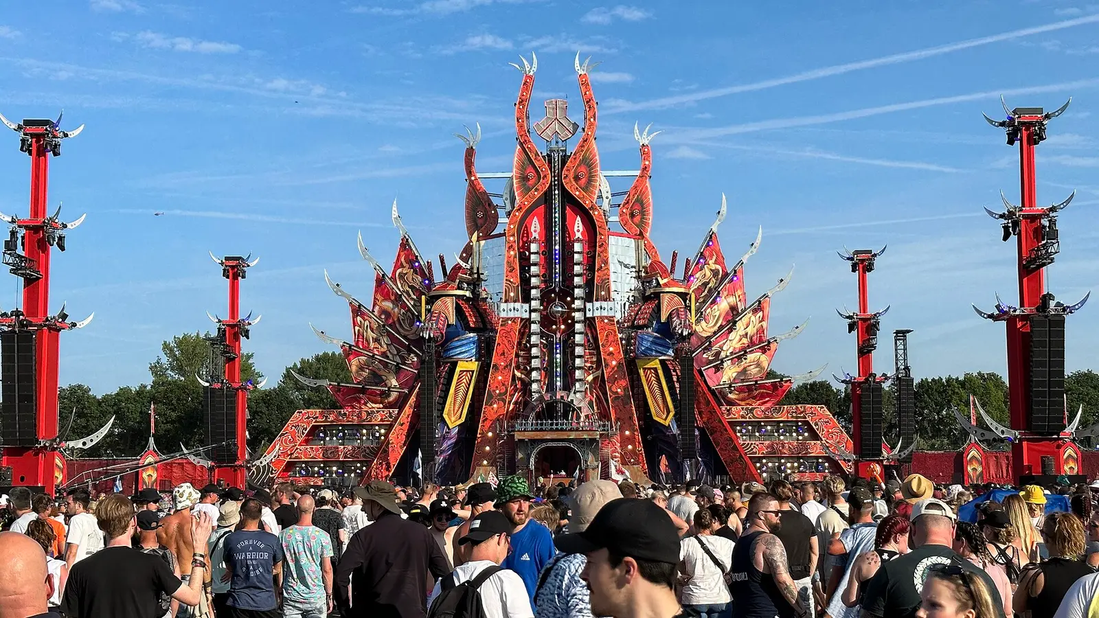 The red and gold main stage and crowd at Defqon.1 in Biddinghuizen under a blue sky