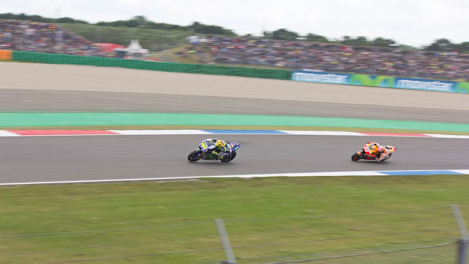 Two MotoGP riders on the track at Assen with the grandstands and crowd beyond the barrier in 2015